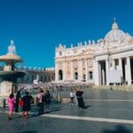 St. Peter's Basilica and fountain in St. Peter's Square, Vatican City, showcasing iconic architecture and tourists.