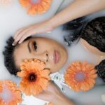 Woman in a black lace top relaxing in a milk bath with orange flowers.